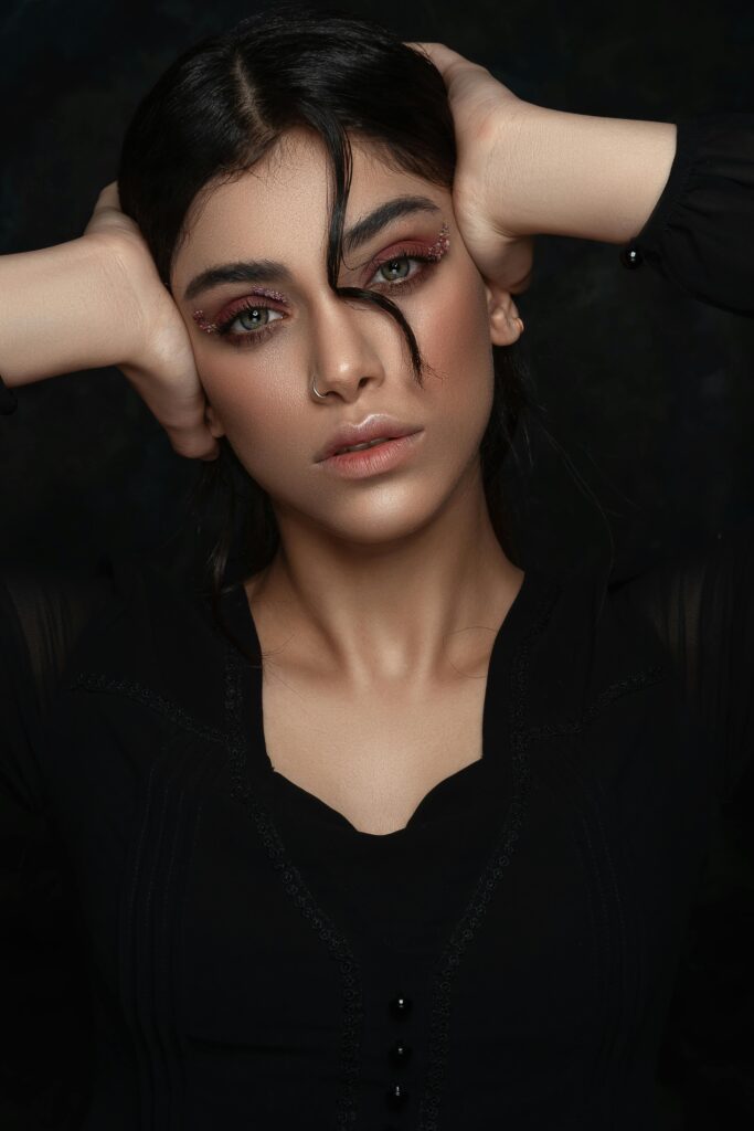 A striking portrait of a woman with dramatic eye makeup and a nose piercing, posing in a studio.